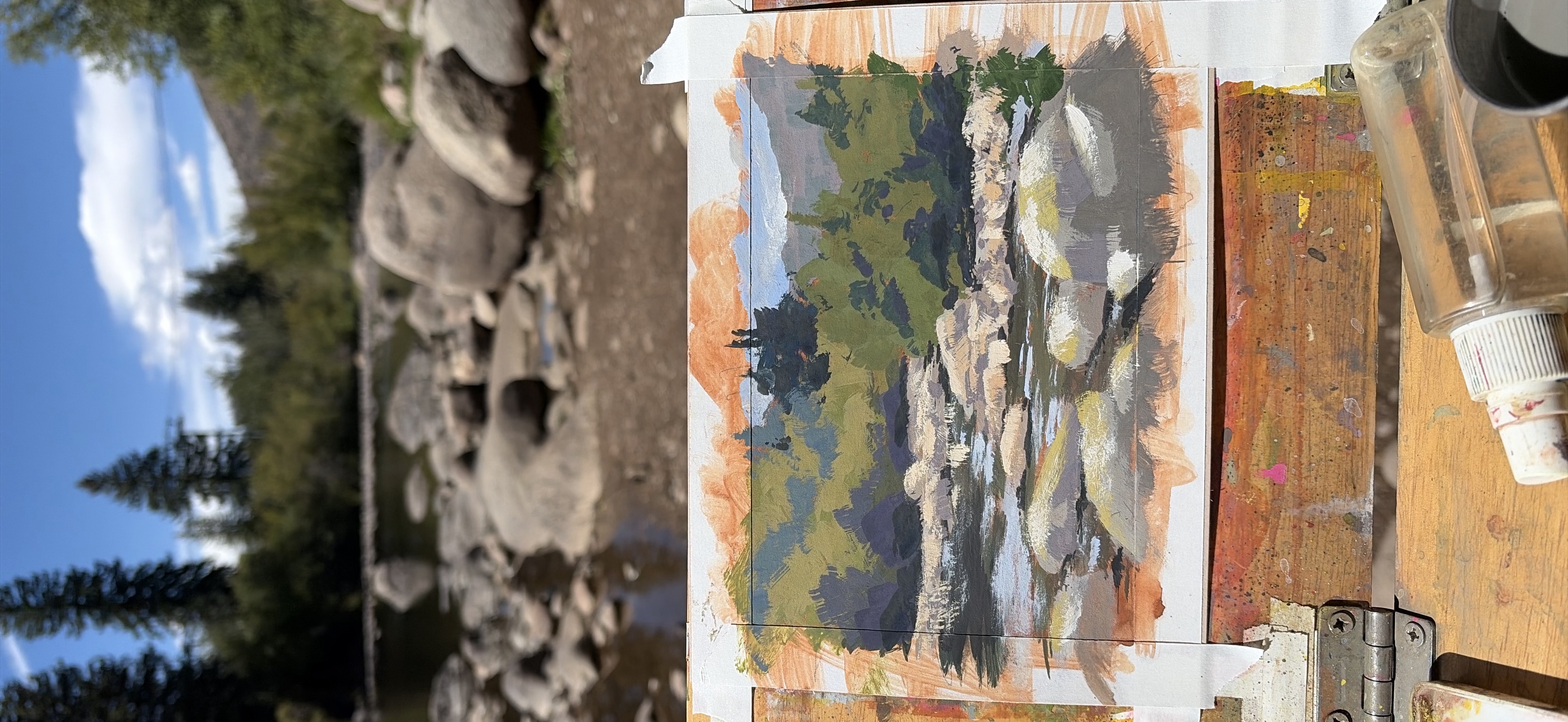 A watercolor painting of a river flowing through a rocky landscape with trees and distant mountains under a blue sky.